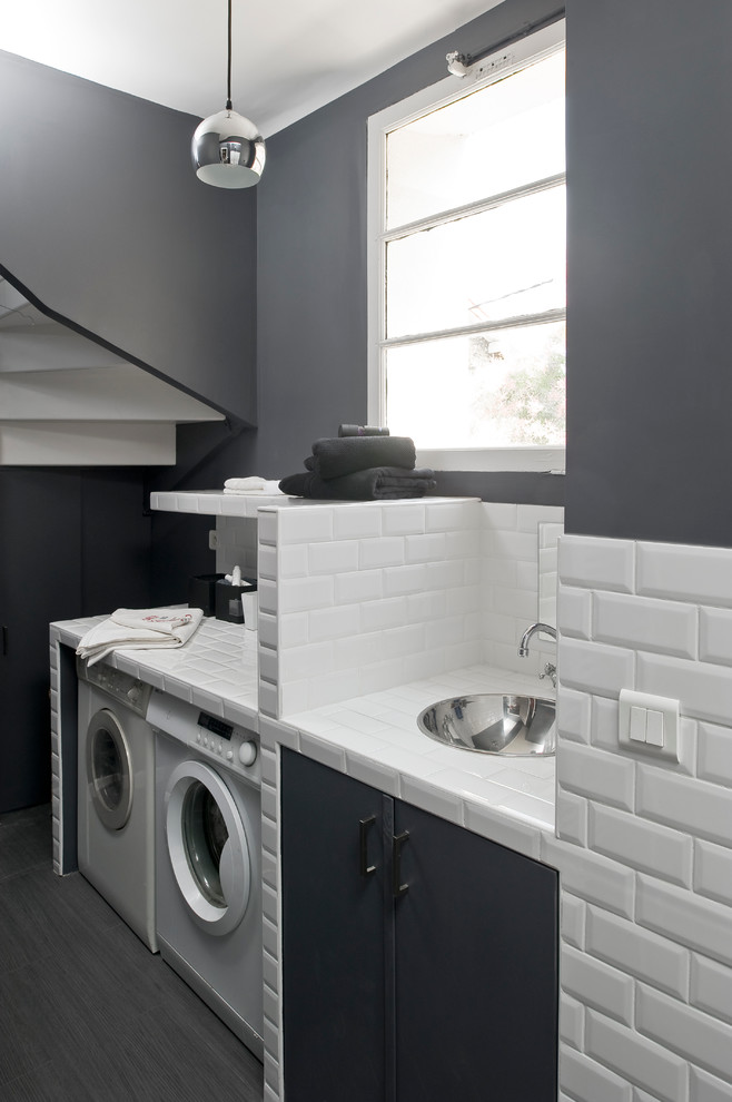 Imagen de cuarto de lavado lineal contemporáneo de tamaño medio con paredes grises, lavadora y secadora juntas, encimera de azulejos, fregadero bajoencimera y suelo de madera pintada