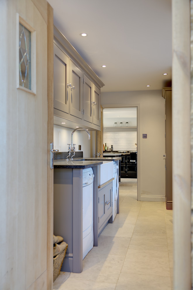 Medium sized classic galley utility room in Hampshire with a belfast sink, flat-panel cabinets, grey cabinets, granite worktops, limestone flooring and a side by side washer and dryer.