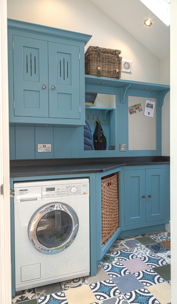 ハンプシャーにある高級な小さなトラディショナルスタイルのおしゃれなランドリールーム (フラットパネル扉のキャビネット、青いキャビネット、御影石カウンター、セラミックタイルの床、左右配置の洗濯機・乾燥機) の写真