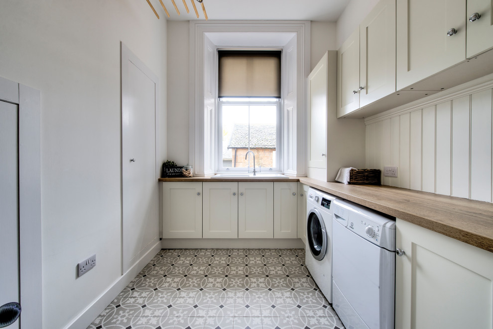 Large classic l-shaped separated utility room in Glasgow with an integrated sink, shaker cabinets, beige cabinets, wood worktops, beige walls, a side by side washer and dryer, multi-coloured floors and brown worktops.