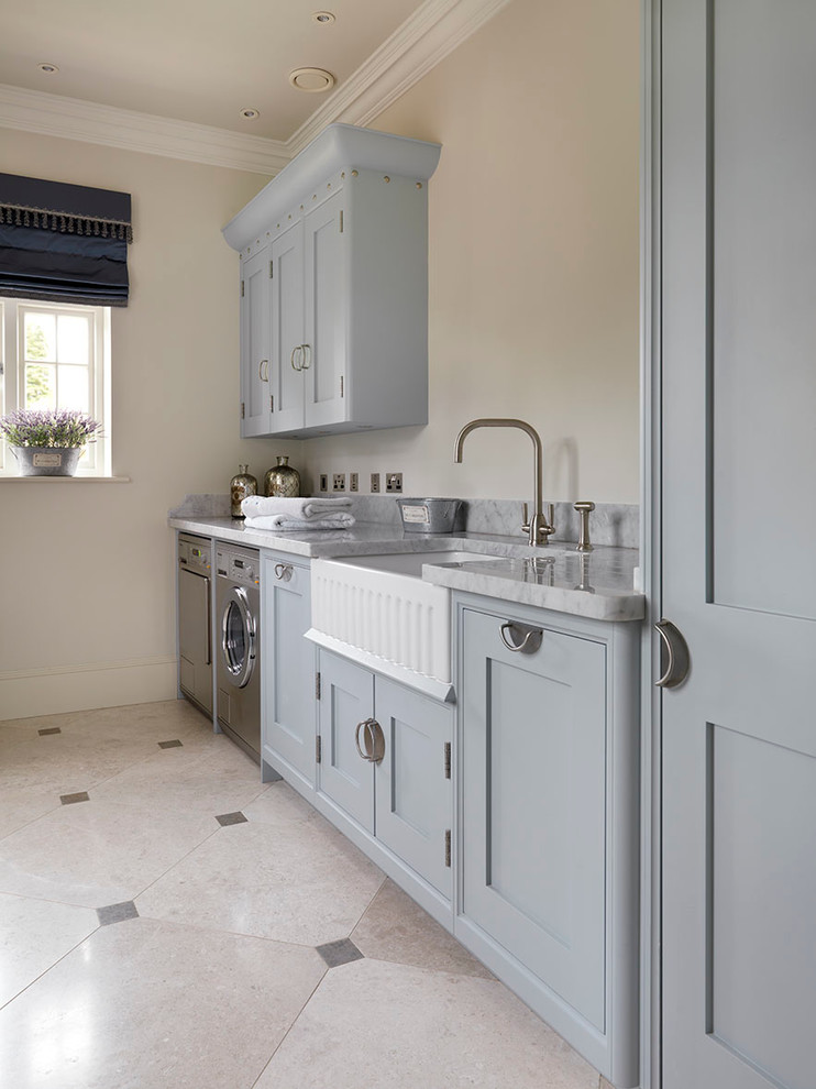 Design ideas for a traditional single-wall separated utility room in Other with limestone flooring, a belfast sink, shaker cabinets, blue cabinets, beige walls, a side by side washer and dryer and grey floors.