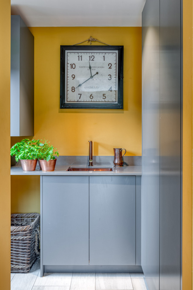 Bild på ett mellanstort funkis grå linjärt grått grovkök, med en nedsänkt diskho, släta luckor, grå skåp, bänkskiva i kvartsit, gula väggar och tvättmaskin och torktumlare byggt in i ett skåp
