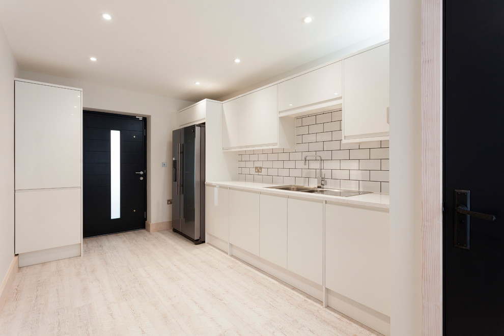 Large modern single-wall utility room in Kent with a double-bowl sink, flat-panel cabinets, white cabinets, quartz worktops, white walls, vinyl flooring and a concealed washer and dryer.