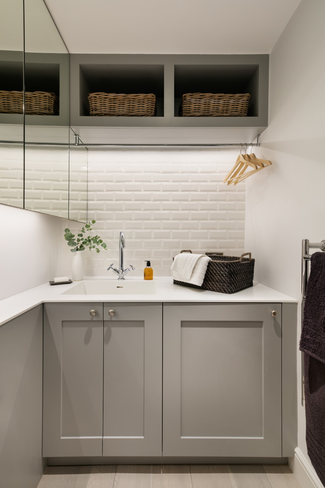 Idéer för en liten tvättstuga, med en nedsänkt diskho, luckor med infälld panel, grå skåp, bänkskiva i koppar, vita väggar, ljust trägolv och tvättmaskin och torktumlare byggt in i ett skåp