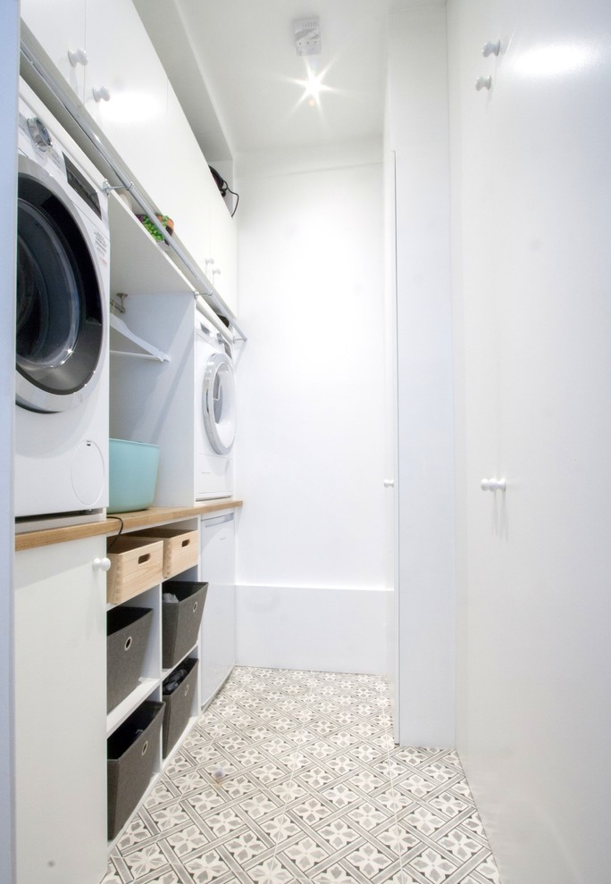 Small contemporary single-wall separated utility room in London with flat-panel cabinets, white cabinets, laminate countertops, a stacked washer and dryer and brown worktops.