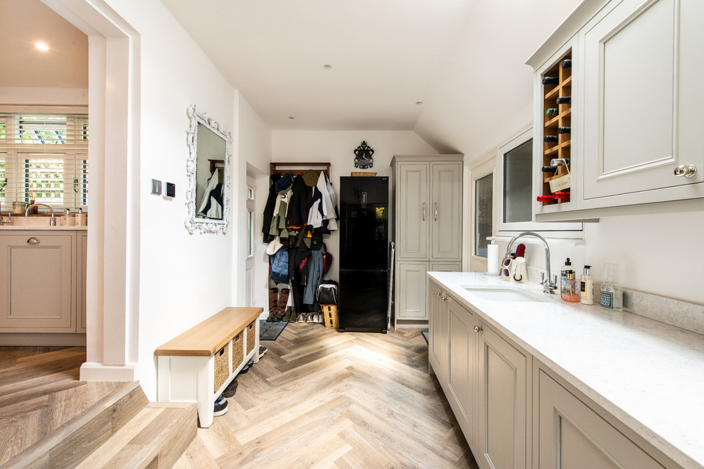 Einzeiliger, Mittelgroßer Klassischer Hauswirtschaftsraum mit Unterbauwaschbecken, Schrankfronten mit vertiefter Füllung, grauen Schränken, weißer Wandfarbe, hellem Holzboden und weißer Arbeitsplatte in Kent