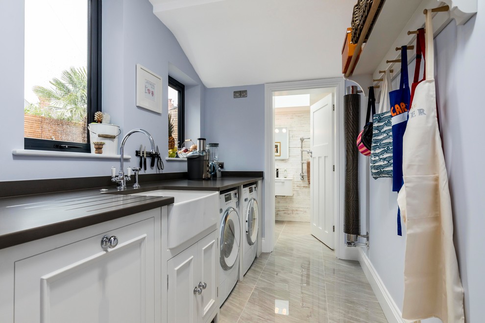 Immagine di una lavanderia classica di medie dimensioni con lavello stile country, ante con bugna sagomata, ante bianche, top in granito, lavatrice e asciugatrice affiancate e pareti blu