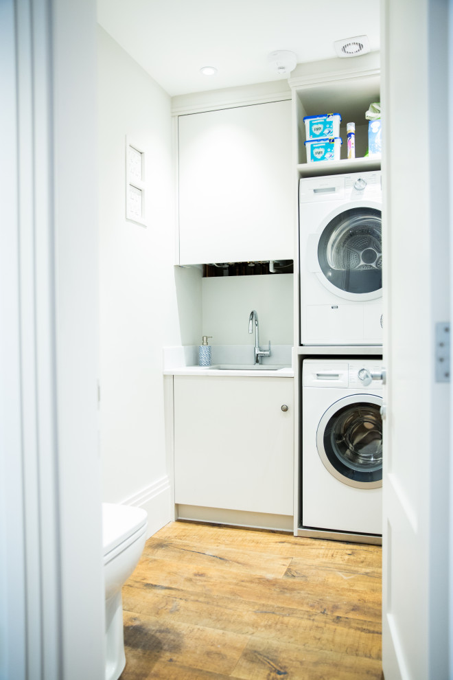 Esempio di una lavanderia multiuso moderna di medie dimensioni con lavello a vasca singola, ante lisce, ante bianche, pareti bianche, parquet scuro, lavatrice e asciugatrice a colonna e pavimento marrone