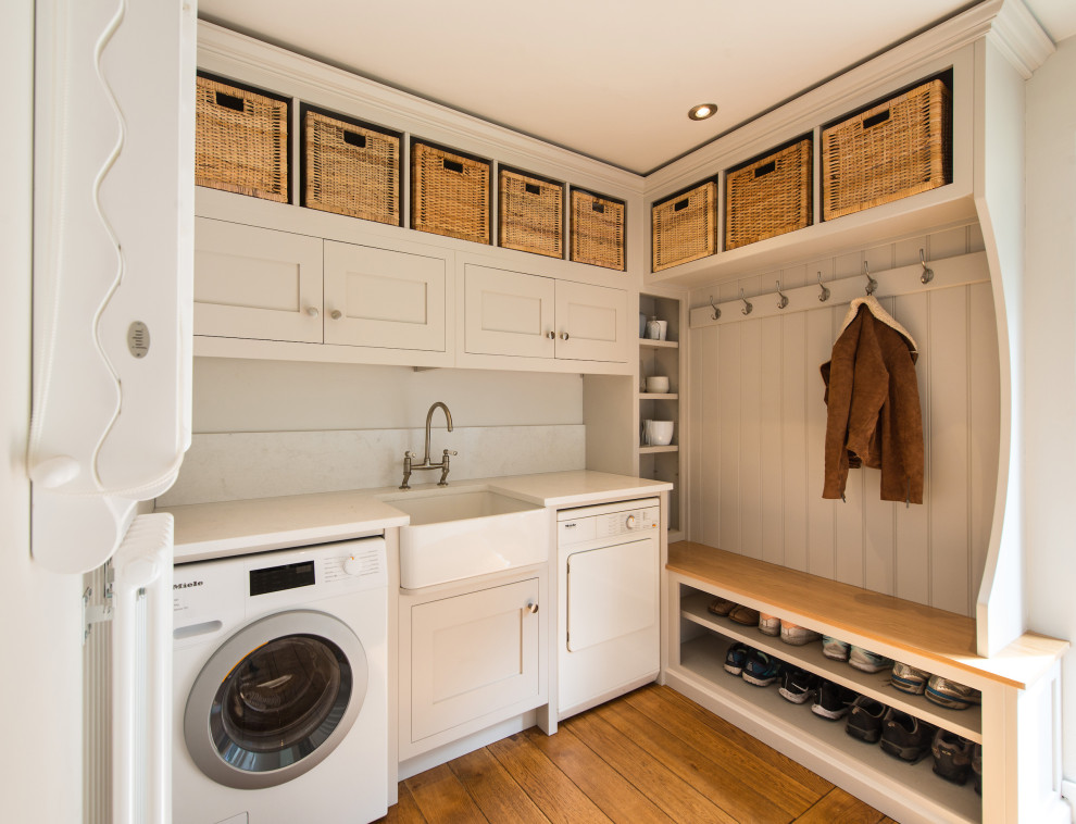 Exempel på en liten lantlig vita vitt tvättstuga, med skåp i shakerstil, vita skåp, bänkskiva i kvartsit, vitt stänkskydd, vita väggar, mellanmörkt trägolv, en tvättmaskin och torktumlare bredvid varandra och brunt golv