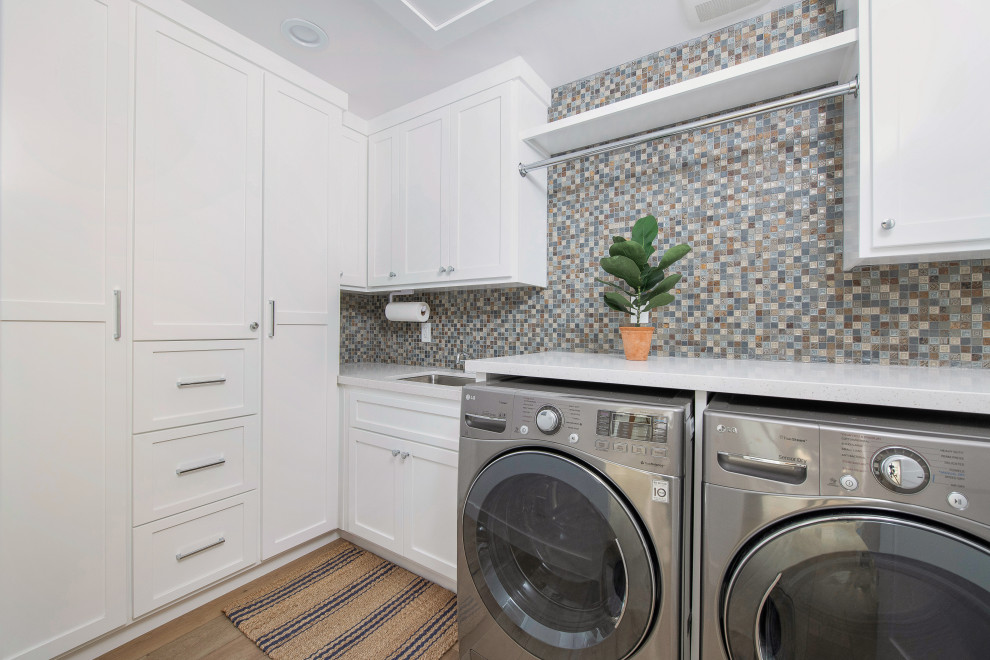 This is an example of a classic l-shaped separated utility room in Orange County with a submerged sink, shaker cabinets, white cabinets, engineered stone countertops, multi-coloured splashback, mosaic tiled splashback, medium hardwood flooring, a side by side washer and dryer, brown floors and white worktops.