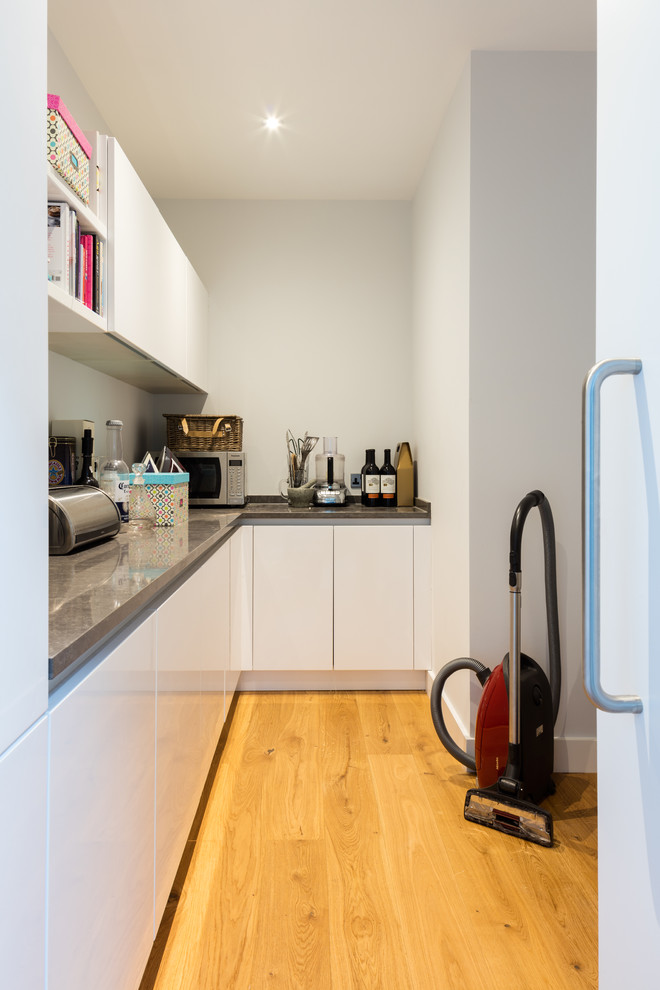 Inspiration for a mid-sized contemporary l-shaped medium tone wood floor and brown floor utility room remodel in London with flat-panel cabinets, white cabinets, quartz countertops and white walls