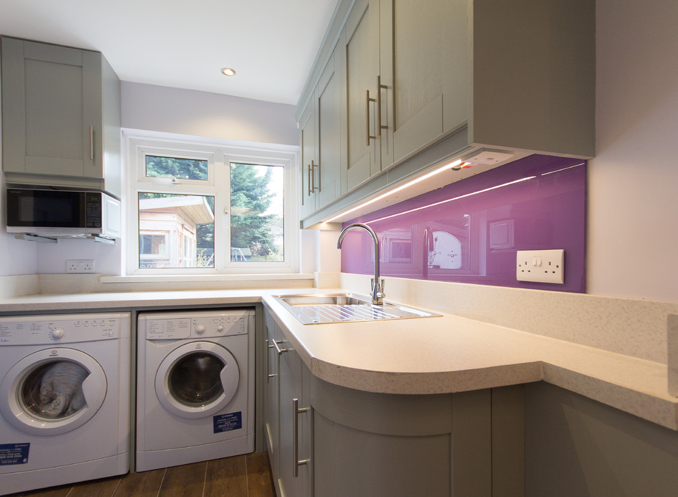 ロンドンにある低価格の小さなモダンスタイルのおしゃれな洗濯室 (L型、シングルシンク、シェーカースタイル扉のキャビネット、グレーのキャビネット、ラミネートカウンター、紫の壁、磁器タイルの床、左右配置の洗濯機・乾燥機) の写真