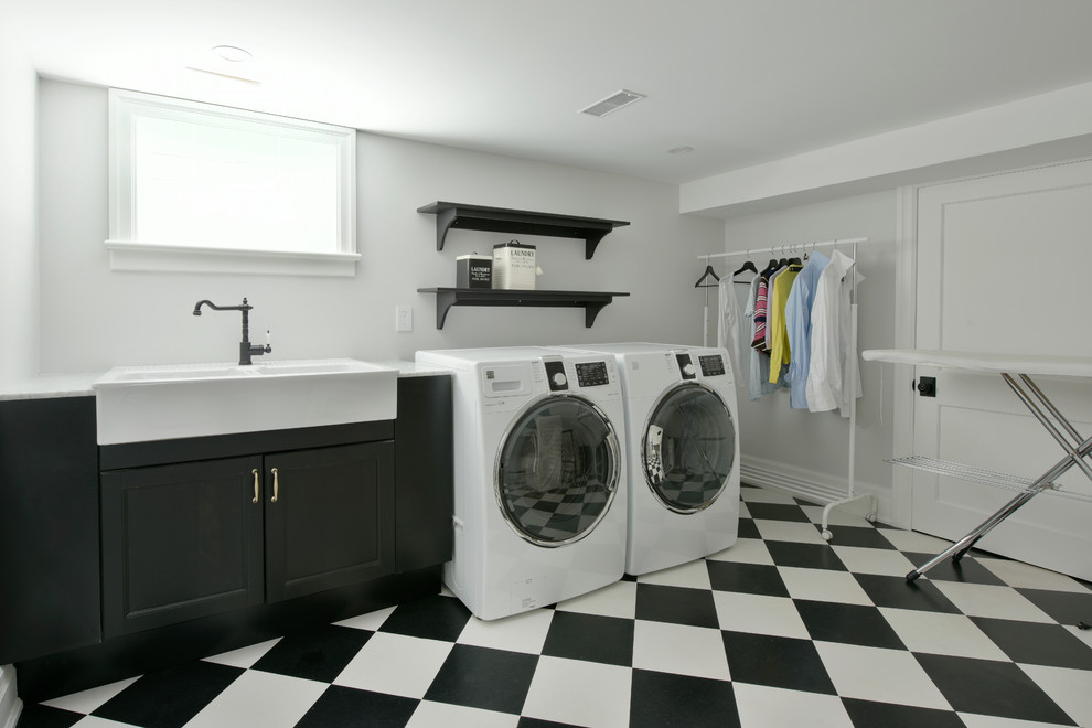 Idéer för att renovera en stor vintage linjär tvättstuga enbart för tvätt, med en rustik diskho, luckor med infälld panel, svarta skåp, marmorbänkskiva, vita väggar, vinylgolv, en tvättmaskin och torktumlare bredvid varandra och flerfärgat golv