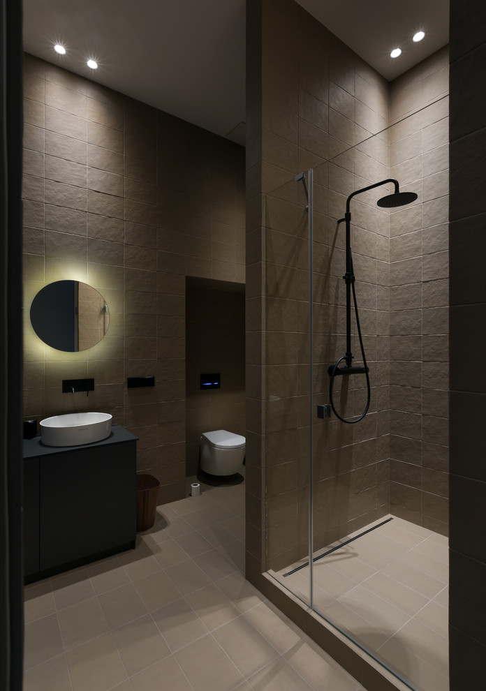 Cette image montre une salle d'eau design avec une vasque, un sol beige, une cabine de douche à porte battante et un plan de toilette noir.
