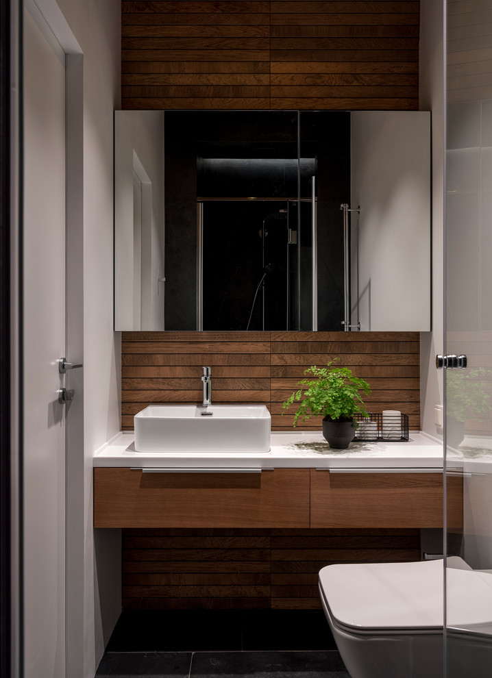 Идея дизайна: ванная комната в современном стиле с плоскими фасадами, фасадами цвета дерева среднего тона, раздельным унитазом, белыми стенами, душевой кабиной, настольной раковиной, черным полом и белой столешницей