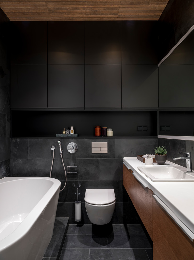 На фото: главная ванная комната в современном стиле с плоскими фасадами, фасадами цвета дерева среднего тона, инсталляцией, черной плиткой, накладной раковиной, черным полом и белой столешницей с