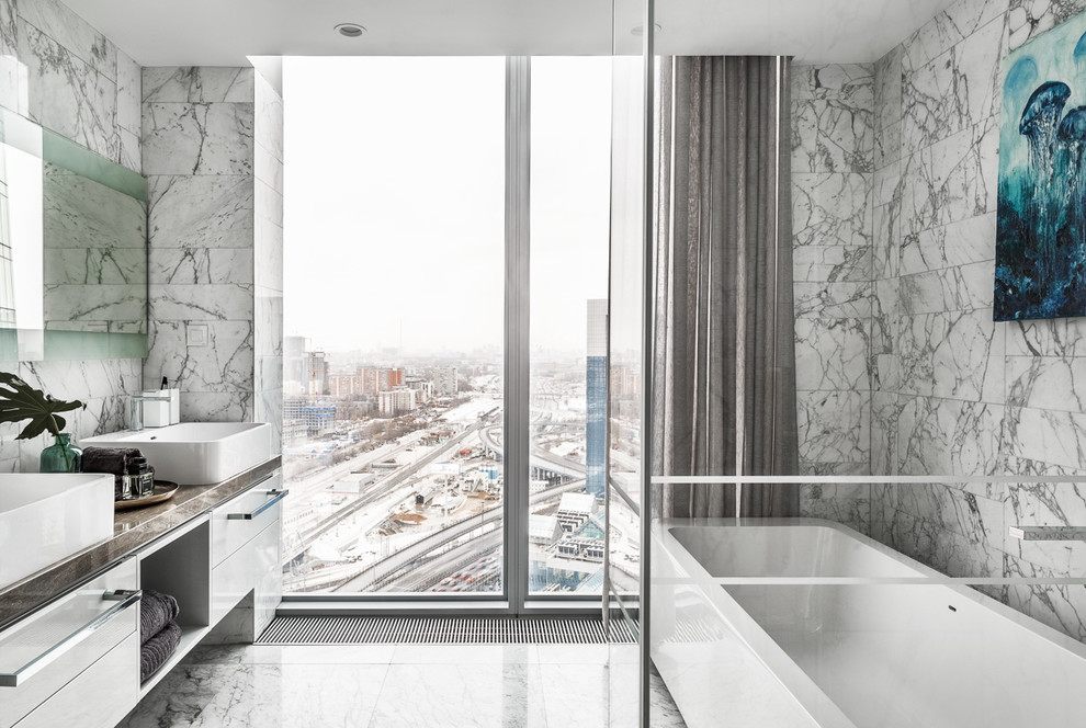 Inredning av ett modernt mellanstort en-suite badrum, med ett fristående badkar, en hörndusch, marmorkakel, marmorgolv, vitt golv, dusch med gångjärnsdörr, släta luckor, vita skåp, grå kakel och ett fristående handfat