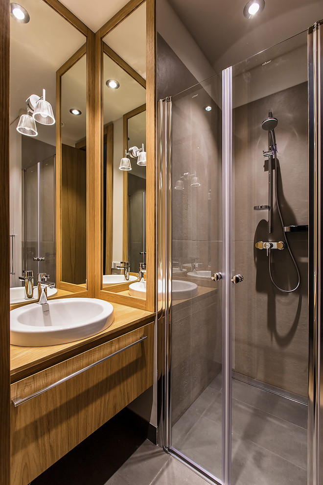 Пример оригинального дизайна: ванная комната в современном стиле с плоскими фасадами, фасадами цвета дерева среднего тона, душем в нише, серой плиткой, душевой кабиной, накладной раковиной, столешницей из дерева, серым полом, душем с распашными дверями и коричневой столешницей