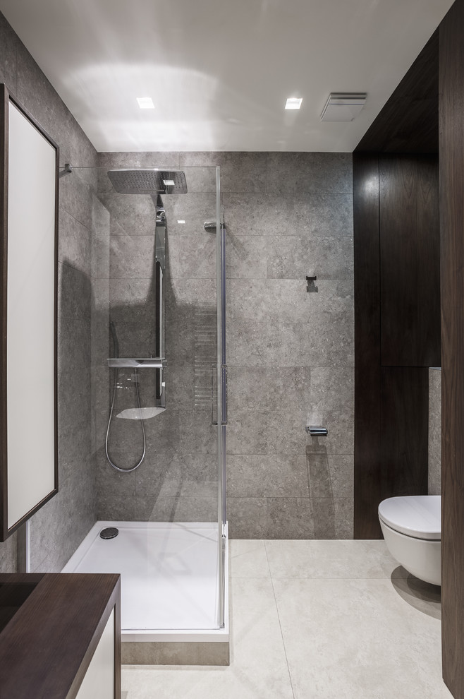 Modern inredning av ett litet badrum med dusch, med släta luckor, vita skåp, en hörndusch, en vägghängd toalettstol, grå kakel, porslinskakel, klinkergolv i porslin och träbänkskiva
