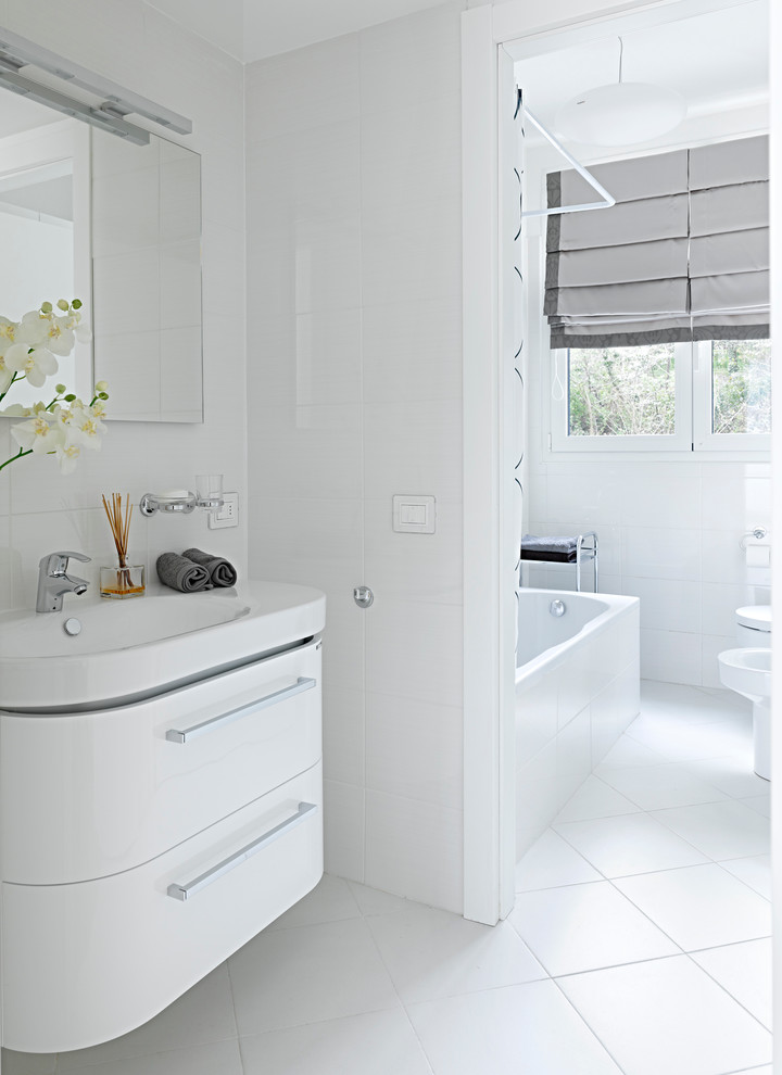 Idées déco pour une salle de bain moderne avec un placard à porte plane, des portes de placard blanches, une baignoire encastrée, WC suspendus, un carrelage blanc, des carreaux de céramique, un mur blanc et un lavabo posé.