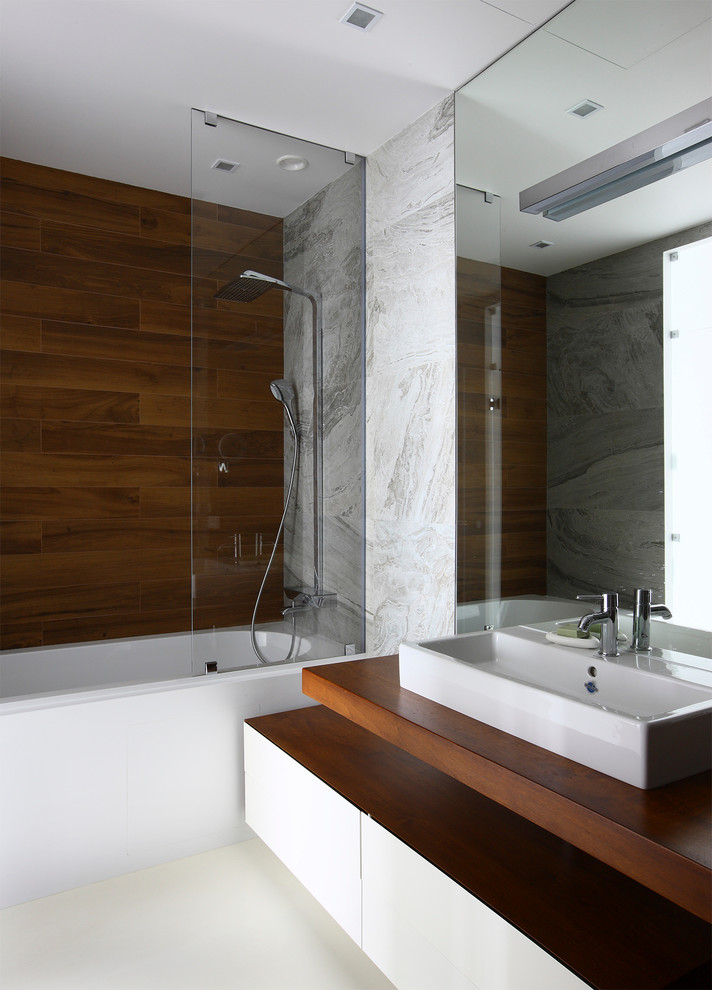 Exempel på ett mellanstort modernt brun brunt en-suite badrum, med släta luckor, vita skåp, ett undermonterat badkar, grå kakel, porslinskakel, träbänkskiva, en dusch/badkar-kombination, ett fristående handfat och med dusch som är öppen