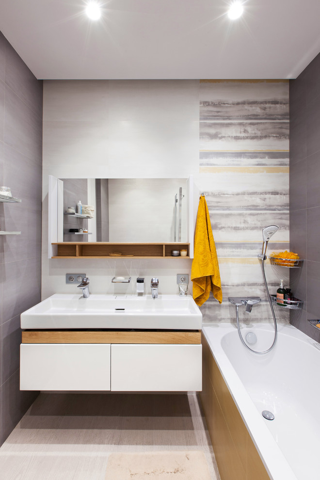 Bild på ett mellanstort funkis en-suite badrum, med släta luckor, vita skåp, en dusch/badkar-kombination, grå kakel, porslinskakel, klinkergolv i porslin, grått golv, ett badkar i en alkov och ett avlångt handfat