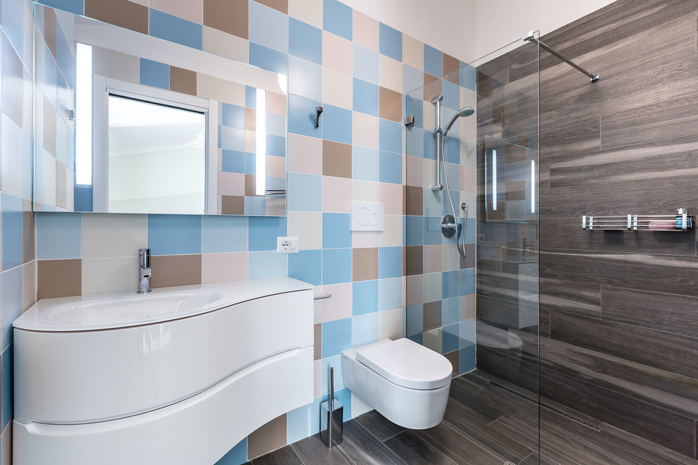 Inredning av ett modernt mellanstort badrum med dusch, med släta luckor, vita skåp, en kantlös dusch, en vägghängd toalettstol, beige kakel, brun kakel, rosa kakel, porslinskakel, vita väggar, klinkergolv i porslin, ett integrerad handfat, bänkskiva i glas och med dusch som är öppen