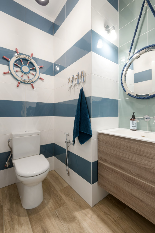Réalisation d'une salle de bain marine en bois clair avec un placard à porte plane, WC séparés, un carrelage bleu, un carrelage blanc, un sol en bois brun, un lavabo intégré, un sol marron, un plan de toilette blanc, meuble simple vasque et meuble-lavabo suspendu.