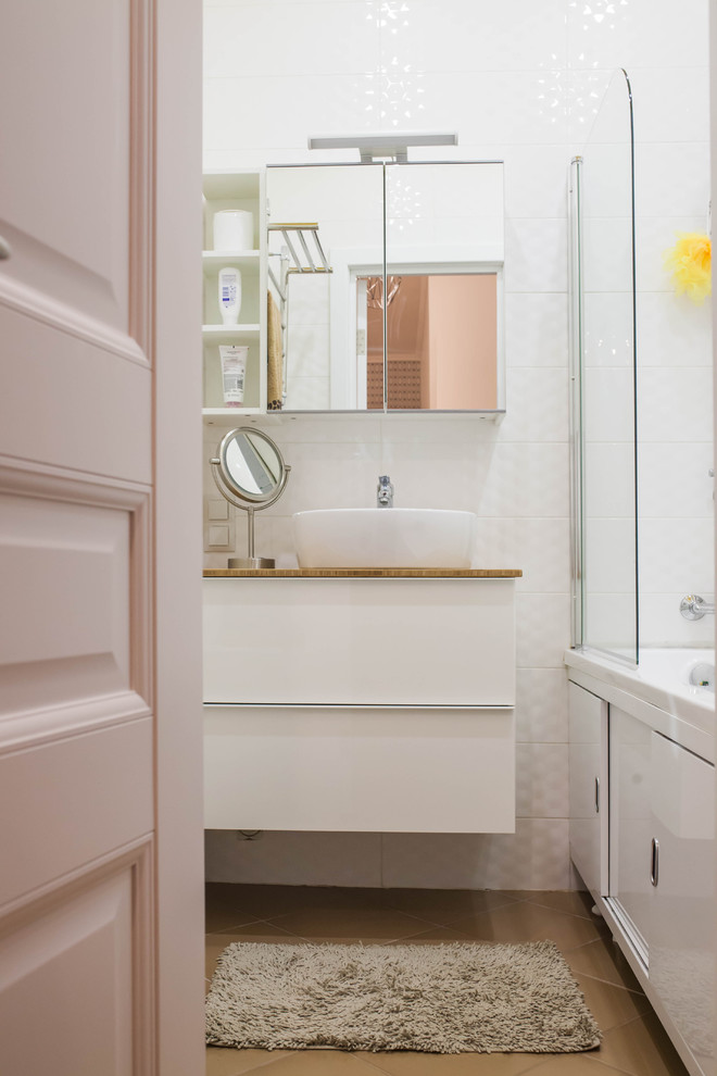 На фото: главная ванная комната в скандинавском стиле с плоскими фасадами, белыми фасадами, ванной в нише, белой плиткой и настольной раковиной