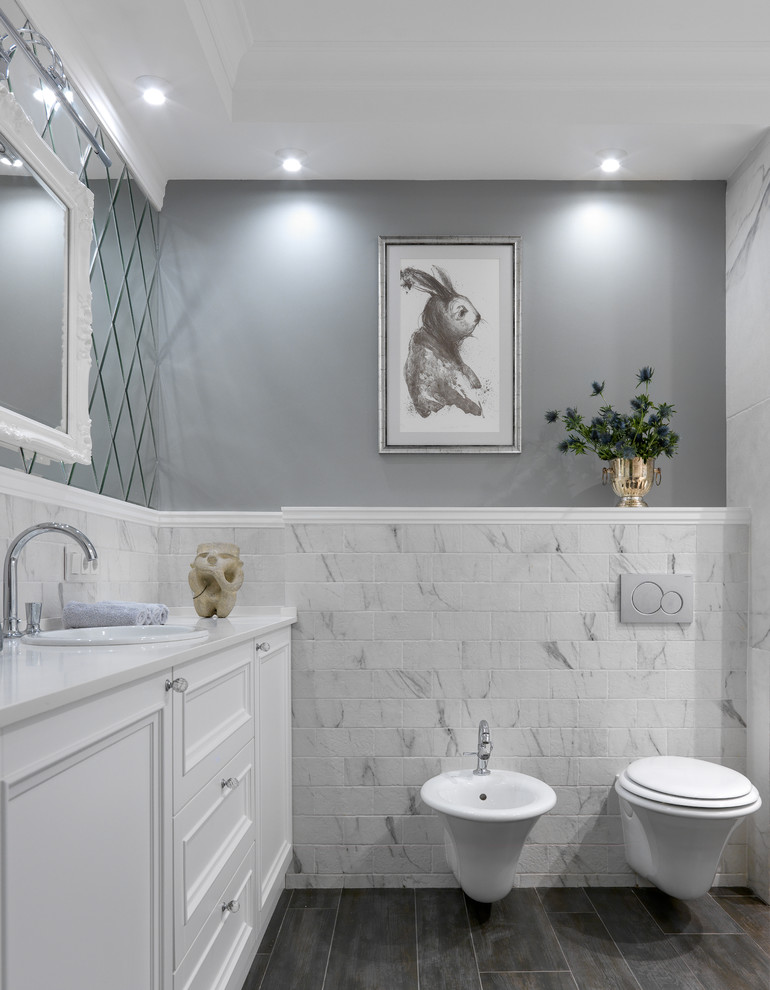 На фото: ванная комната в стиле неоклассика (современная классика) с фасадами с утопленной филенкой, белыми фасадами, инсталляцией, белой плиткой, серыми стенами, накладной раковиной, серым полом и белой столешницей