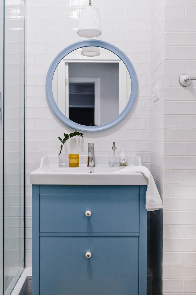 На фото: маленькая ванная комната в скандинавском стиле с плоскими фасадами, синими фасадами, белой плиткой, керамической плиткой, душевой кабиной, монолитной раковиной и душем с раздвижными дверями для на участке и в саду