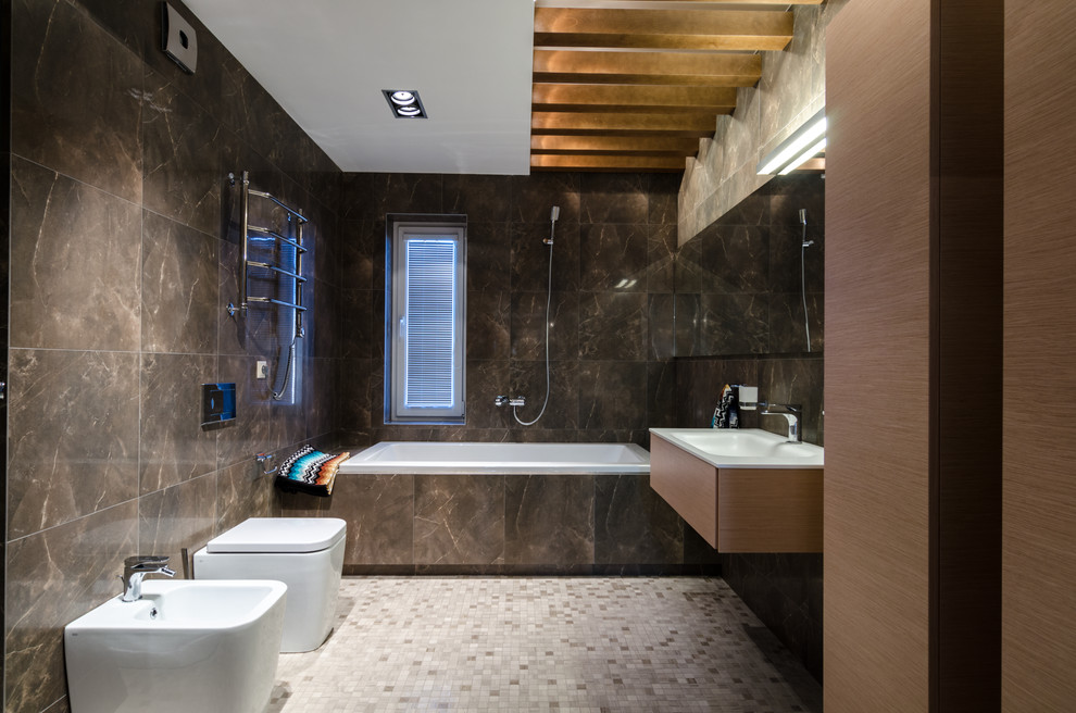Bild på ett funkis en-suite badrum, med släta luckor, skåp i mellenmörkt trä, ett badkar i en alkov, en dusch/badkar-kombination, en toalettstol med separat cisternkåpa, brun kakel, mosaikgolv, ett integrerad handfat och grått golv