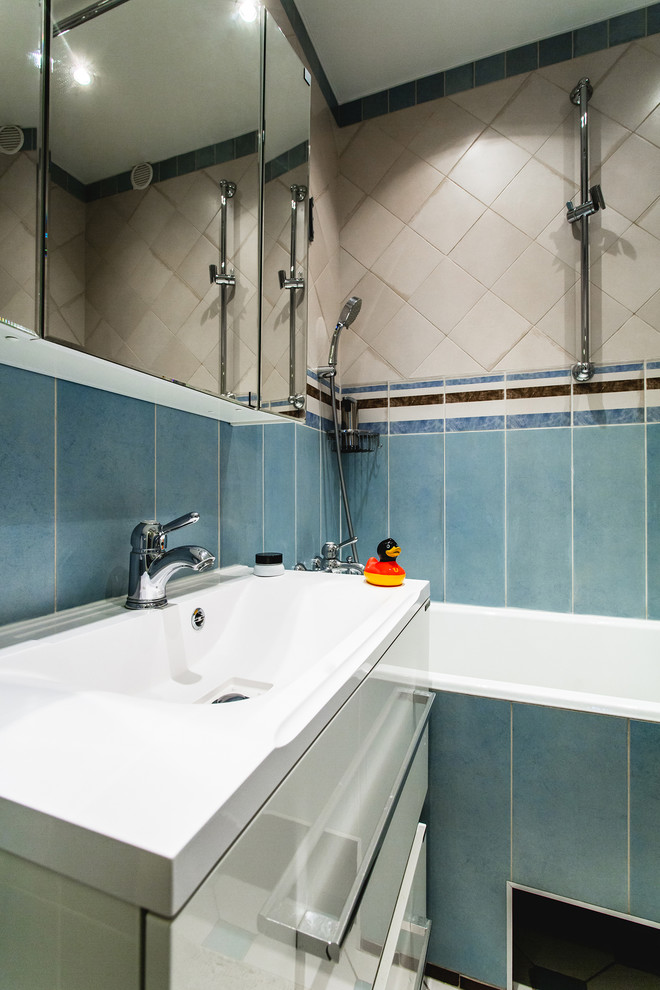 Immagine di una stanza da bagno design con ante lisce, ante bianche, vasca/doccia, vasca da incasso, lavabo integrato, pareti blu e piastrelle blu