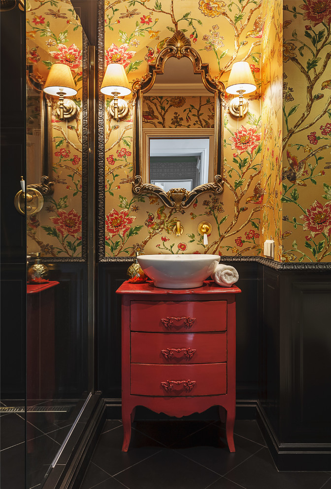 Cette image montre une salle de bain bohème avec un placard à porte plane, des portes de placard rouges, un carrelage noir, un mur jaune, une vasque et un sol noir.