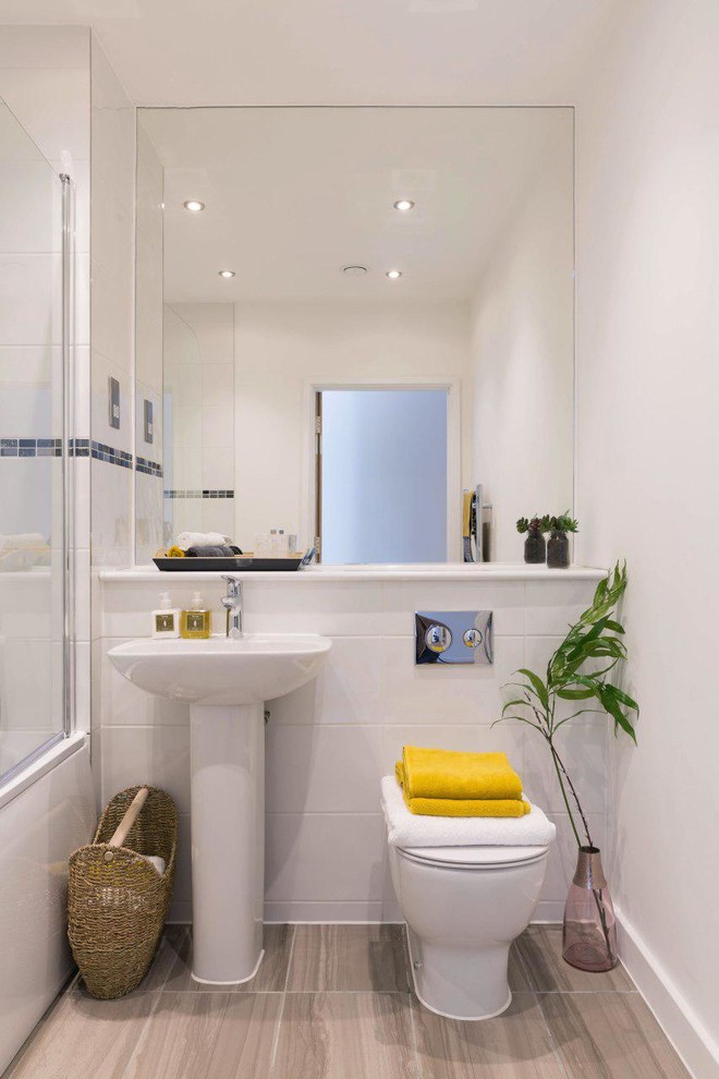 Modern inredning av ett badrum med dusch, med ett badkar i en alkov, en toalettstol med hel cisternkåpa, vit kakel, vita väggar, ett piedestal handfat, brunt golv och klinkergolv i keramik