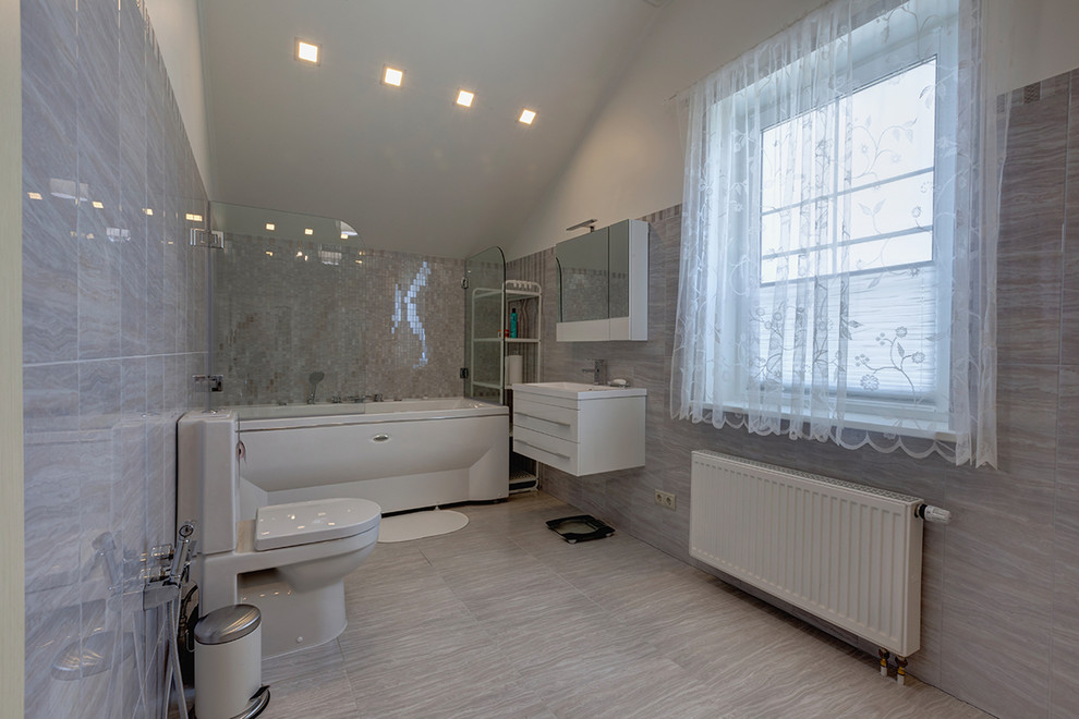 Inspiration pour une grande salle de bain principale design avec un placard à porte plane, des portes de placard blanches, WC séparés, un carrelage gris, un mur gris, un bain bouillonnant et un lavabo intégré.