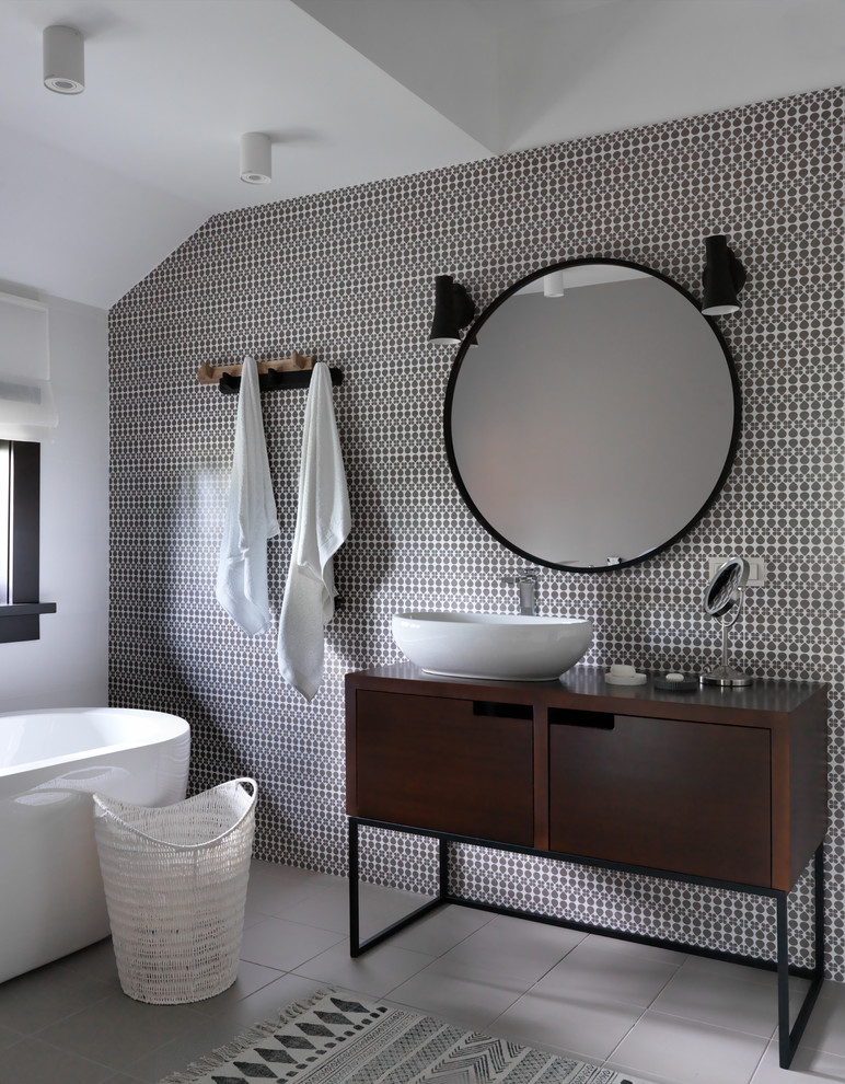 Modern inredning av ett mellanstort brun brunt en-suite badrum, med ett fristående badkar, keramikplattor, klinkergolv i porslin, ett fristående handfat, träbänkskiva, grått golv, släta luckor, skåp i mörkt trä, vita väggar och svart och vit kakel