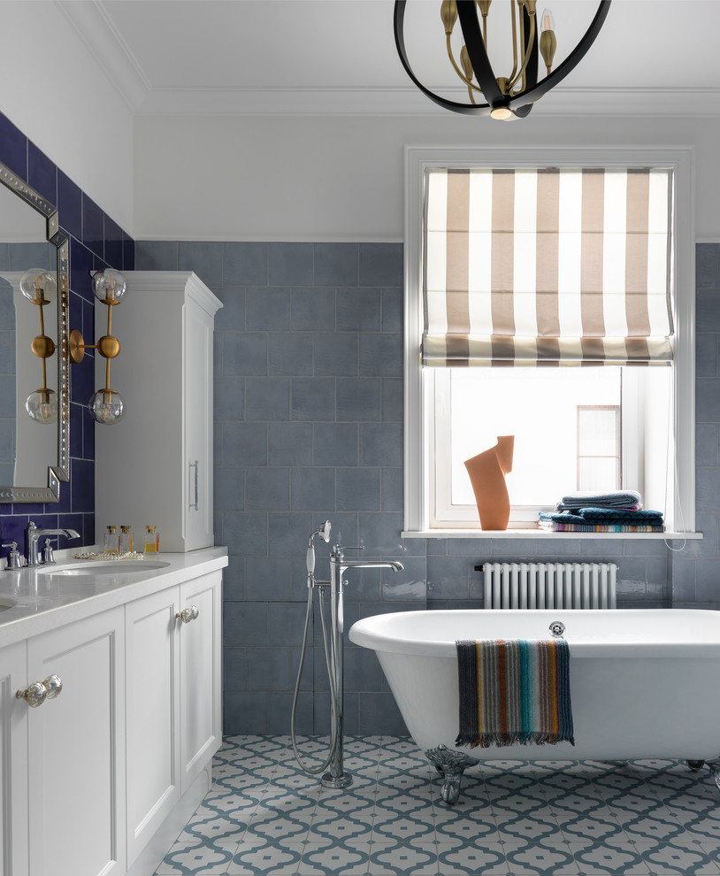 На фото: ванная комната в стиле неоклассика (современная классика) с фасадами с утопленной филенкой, белыми фасадами, ванной на ножках, синей плиткой, белыми стенами, врезной раковиной, разноцветным полом и белой столешницей с