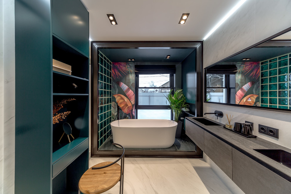 Cette image montre une salle de bain principale design avec une baignoire indépendante, un carrelage vert, un lavabo encastré et un plan de toilette gris.