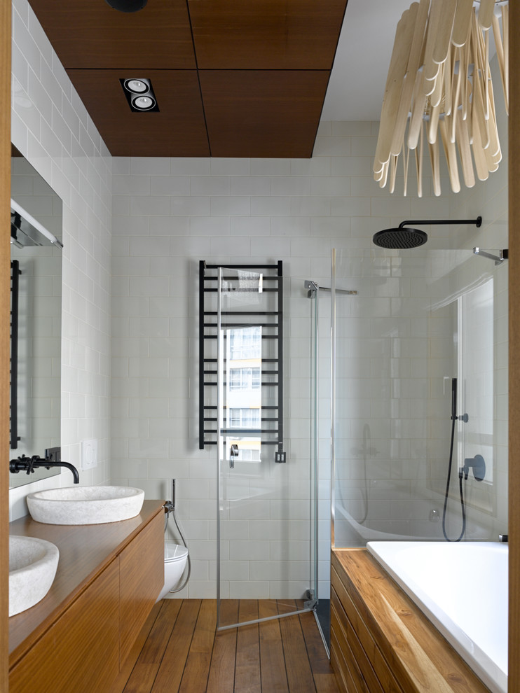 Cette image montre une salle de bain design en bois brun avec un placard à porte plane, une baignoire posée, une douche d'angle, un carrelage blanc, un mur blanc, un sol en bois brun, une vasque, un plan de toilette en bois, un sol marron, une cabine de douche à porte battante et un plan de toilette marron.