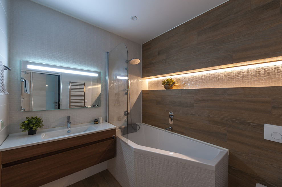 Modern inredning av ett badrum, med en dusch/badkar-kombination, en vägghängd toalettstol, brun kakel, porslinskakel, klinkergolv i porslin och ett hörnbadkar