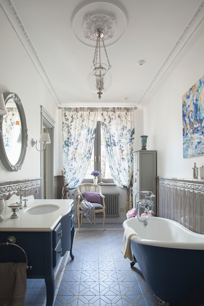 Пример оригинального дизайна: главная ванная комната в классическом стиле с синими фасадами, ванной на ножках, белыми стенами, полом из керамической плитки, врезной раковиной, мраморной столешницей, разноцветным полом и фасадами с выступающей филенкой