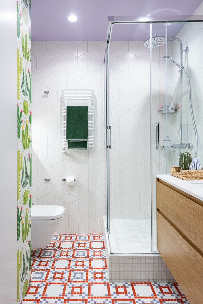 Idéer för ett litet modernt vit badrum för barn, med luckor med infälld panel, skåp i mellenmörkt trä, en vägghängd toalettstol, vit kakel, mosaik, vita väggar, mosaikgolv, ett undermonterad handfat, bänkskiva i akrylsten, flerfärgat golv och dusch med skjutdörr