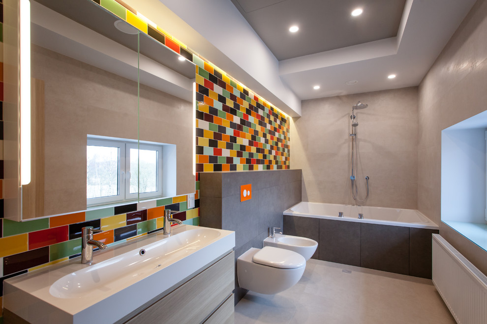 Foto på ett mellanstort funkis badrum för barn, med ett platsbyggt badkar, en dusch/badkar-kombination, en vägghängd toalettstol, flerfärgad kakel, keramikplattor, flerfärgade väggar, klinkergolv i porslin, ett avlångt handfat och beiget golv