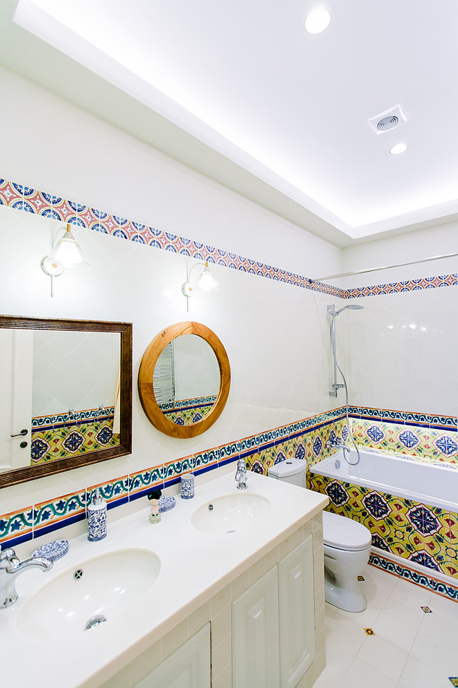 モスクワにある地中海スタイルのおしゃれなマスターバスルーム (レイズドパネル扉のキャビネット、白いキャビネット、アルコーブ型浴槽、シャワー付き浴槽	、分離型トイレ、白いタイル、マルチカラーのタイル、アンダーカウンター洗面器、シャワーカーテン) の写真