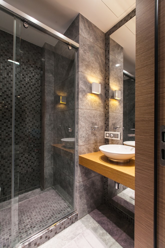 Foto på ett funkis brun badrum med dusch, med en dusch i en alkov, grå kakel, ett fristående handfat, skåp i ljust trä, en vägghängd toalettstol, porslinskakel, grå väggar, klinkergolv i porslin, träbänkskiva, grått golv och dusch med skjutdörr