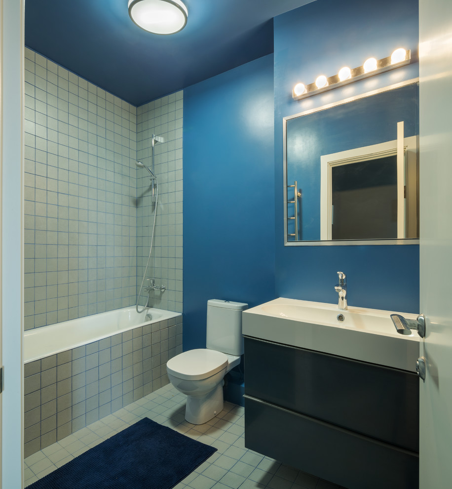 Bild på ett funkis en-suite badrum, med släta luckor, svarta skåp, ett badkar i en alkov, en dusch/badkar-kombination, en toalettstol med separat cisternkåpa, vit kakel, blå väggar och ett integrerad handfat
