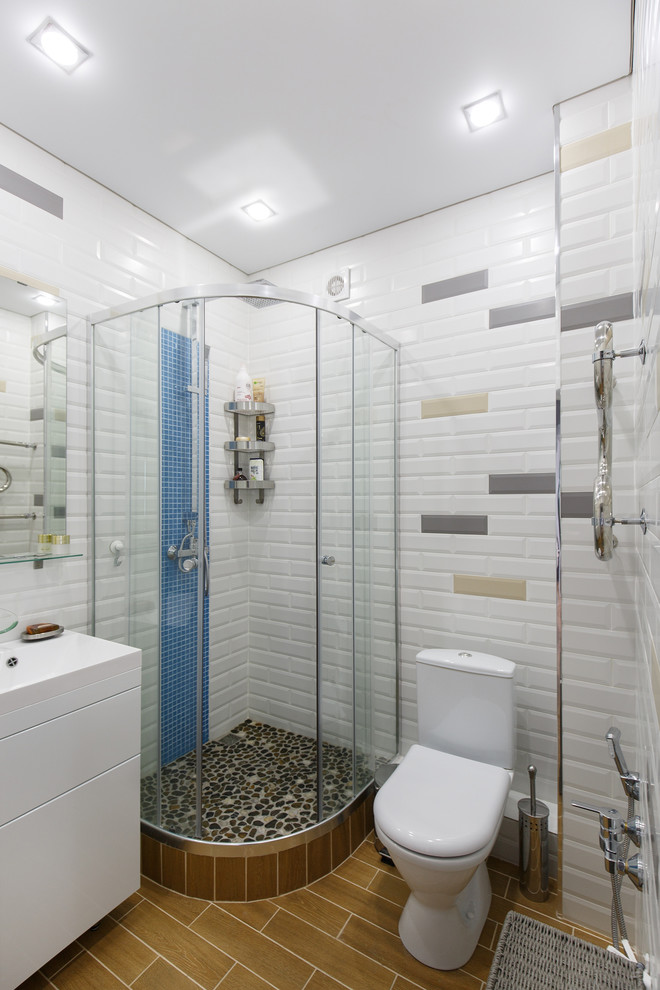 Foto på ett litet funkis badrum med dusch, med släta luckor, vita skåp, en hörndusch, en toalettstol med separat cisternkåpa, vit kakel, tunnelbanekakel, ett integrerad handfat, brunt golv och dusch med skjutdörr