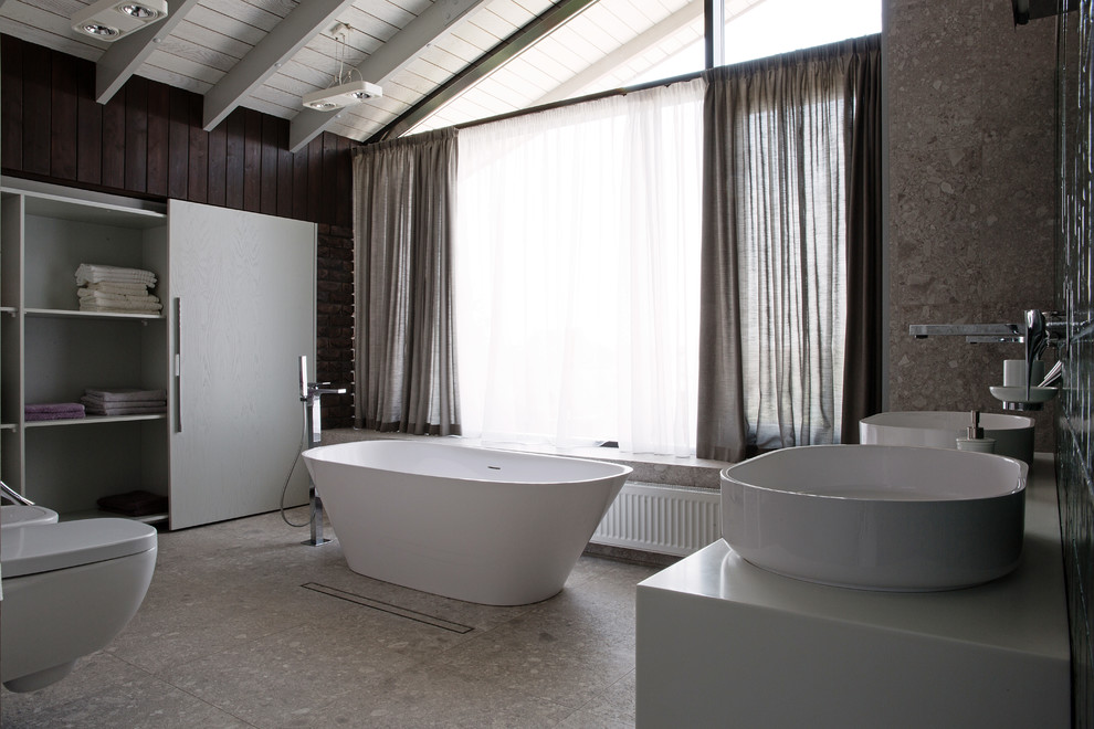 На фото: огромная главная ванная комната в современном стиле с отдельно стоящей ванной, фасадами с выступающей филенкой, серыми фасадами, душевой комнатой, писсуаром, коричневой плиткой, терракотовой плиткой, серыми стенами, мраморным полом, раковиной с пьедесталом, столешницей из искусственного камня, серым полом и душем с раздвижными дверями