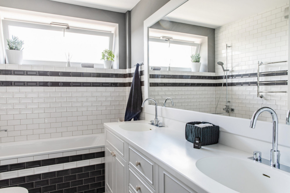 Пример оригинального дизайна: ванная комната среднего размера в стиле неоклассика (современная классика) с белыми фасадами, ванной в нише, душевой кабиной, белой столешницей, керамической плиткой, тумбой под две раковины, встроенной тумбой, фасадами с утопленной филенкой, душем над ванной, черно-белой плиткой, серыми стенами, монолитной раковиной и открытым душем